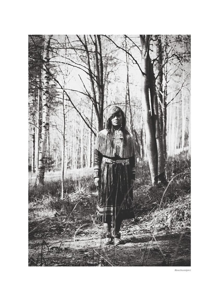 Samisk kvinna står i en enslig skog, hon backar sapmi